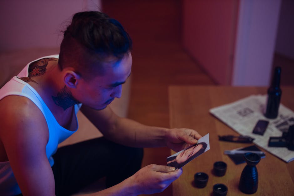 A man with tattoos looks at a photo on a dimly lit table with assorted items.