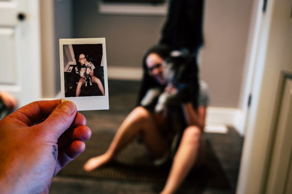 A hand holds a Polaroid of a woman with a dog while she sits behind, blurred.