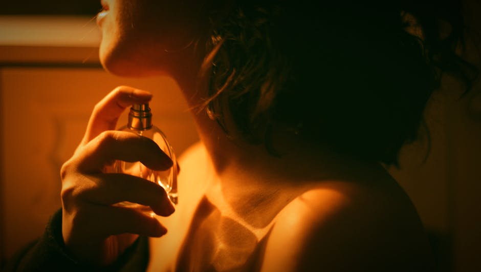 Artistic close-up of a woman applying perfume with warm lighting.