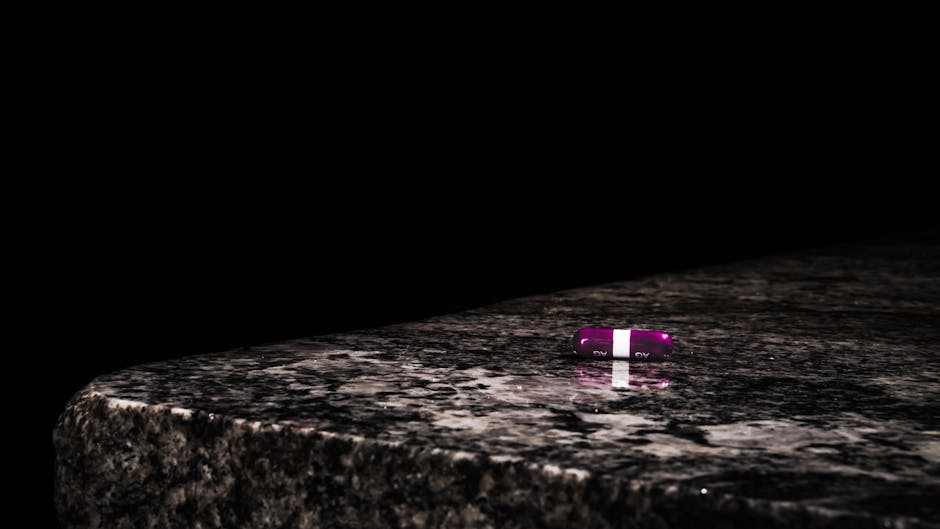 Close-up of a purple capsule resting on a dark marble surface against a black background.