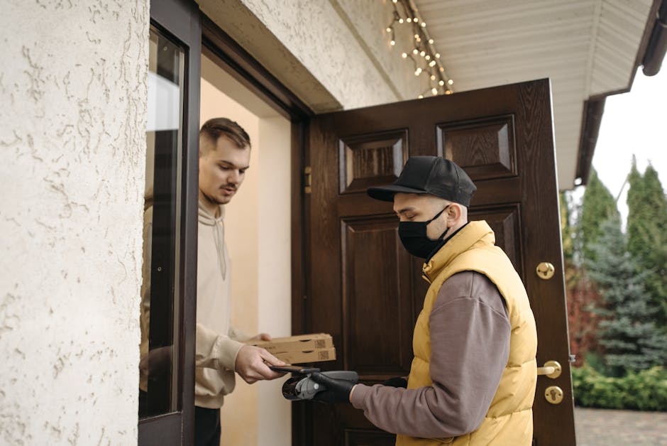Courier wearing a mask hands a package to a man at home. Safe delivery service.