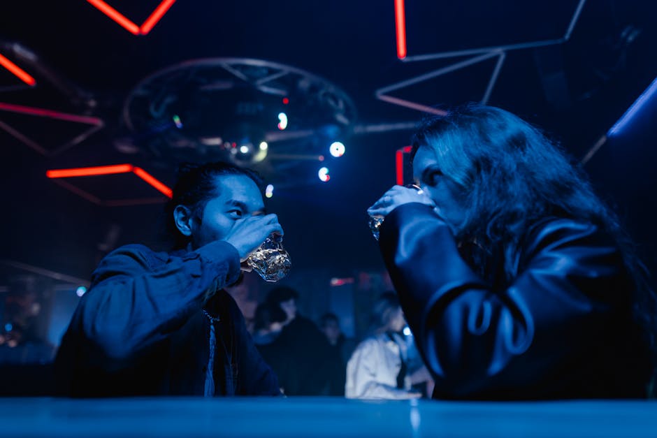 Two friends enjoying drinks at a vibrant nightclub, surrounded by neon lights and music.
