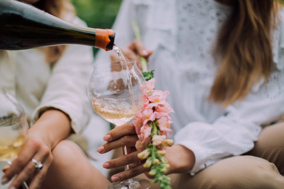 Close-up of wine being poured into a glass with flowers held, capturing a serene outdoor setting.