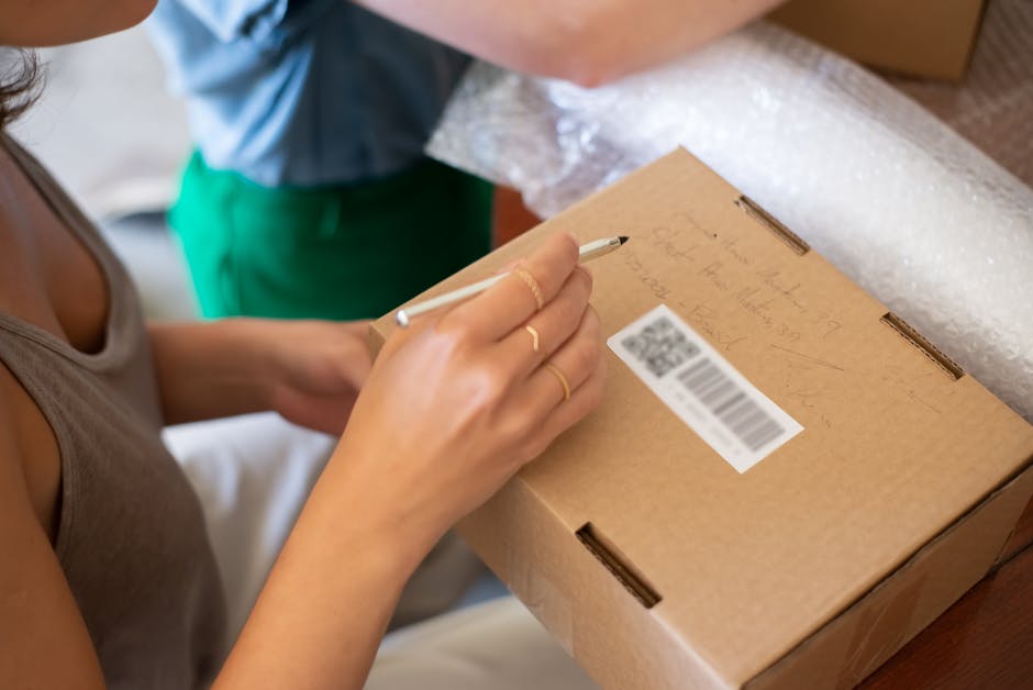 Close-up of a woman writing on a cardboard box, preparing for shipping.