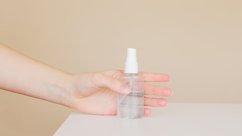 A person holding a transparent sanitizer bottle, symbolizing hygiene and cleanliness indoors.
