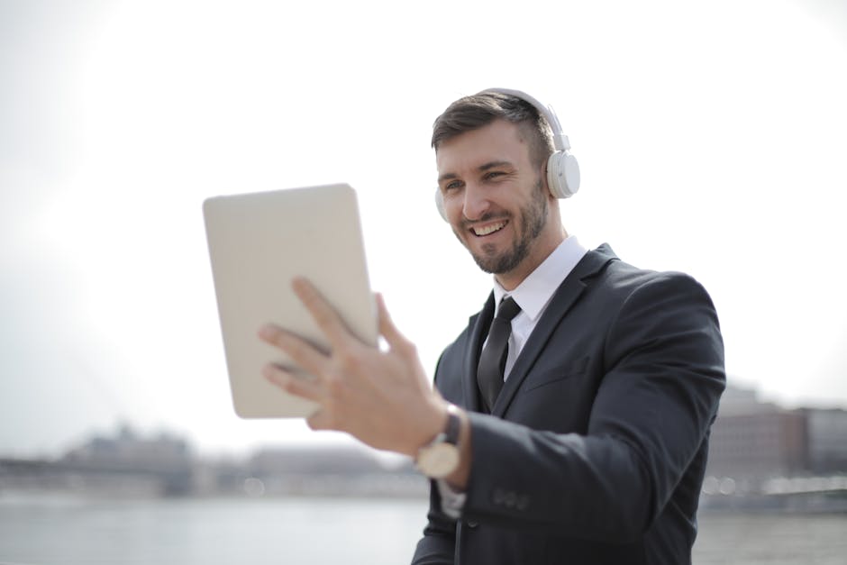 Professional man in a suit smiling while using a tablet with headphones outdoors.