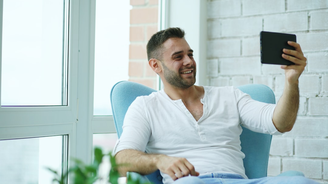 Man sitting in chair taking a selfie with tablet