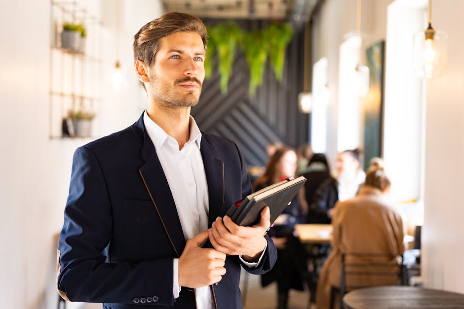 Confident man in a blue suit holding notebooks in a modern cafe setting.