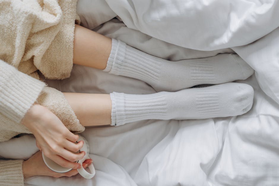 Relaxing indoors wrapped in white linens and warm clothing, enjoying a soothing moment with a cup.