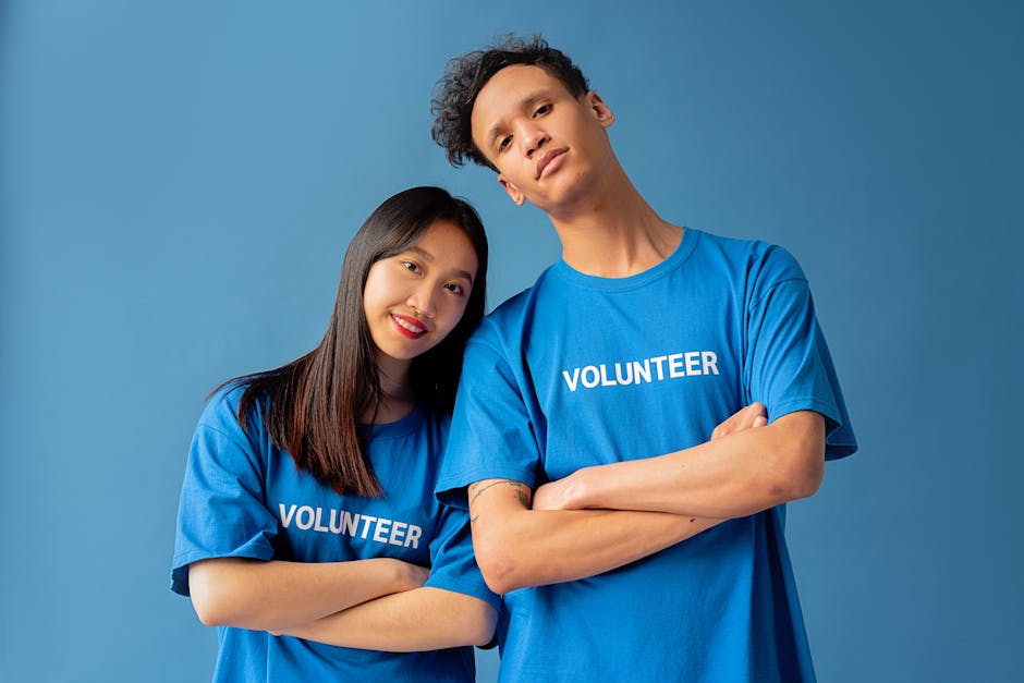 Two young volunteers in blue shirts pose confidently against a blue backdrop.