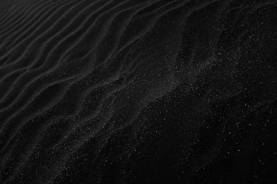 Textured black sand with ripples resembling dunes, creating a dark, abstract aesthetic.