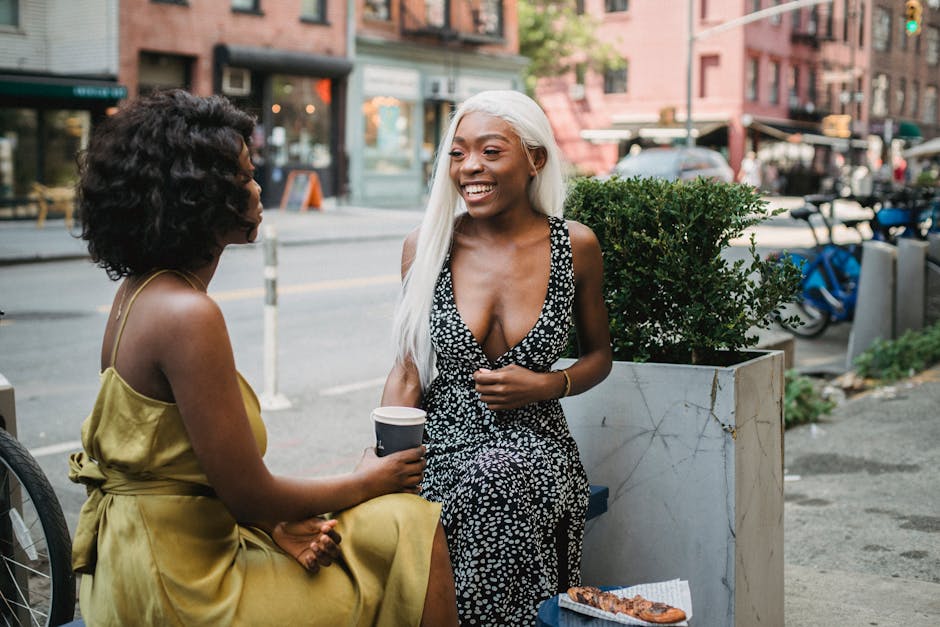 Two women sitting at a cafe outdoors, engaged in a cheerful conversation over coffee.