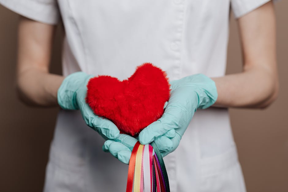 A nurse in gloves holds a red heart with rainbow strings, symbolizing love and healthcare.