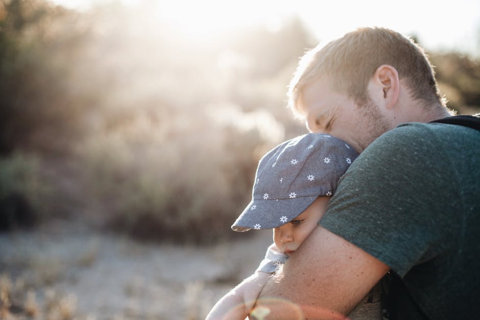 A father lovingly embraces his baby outdoors on a sunny day. Perfect for Father's Day themes.