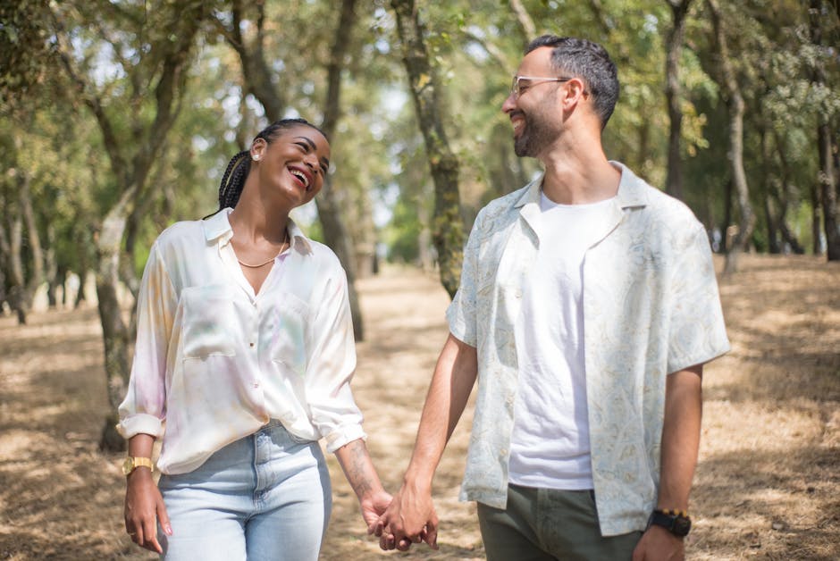 Smiling couple holding hands in a sunlit park, enjoying a cheerful day outdoors.