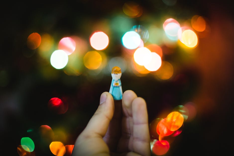 Close-up of a hand holding a small toy figure with colorful bokeh lights in the background.