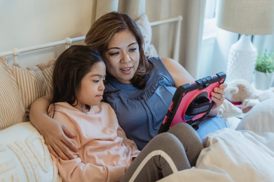 A mother and daughter share a moment, watching a tablet together in a cozy bedroom setting.
