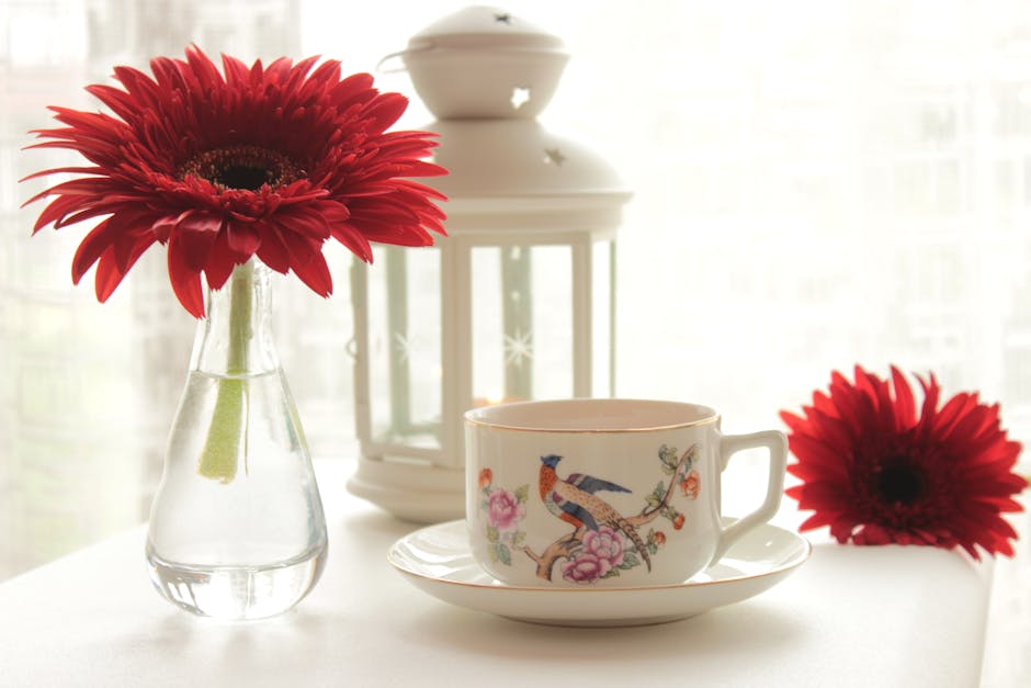 A serene indoor tea setup featuring a floral cup, red gerbera flowers, and a decorative lantern.