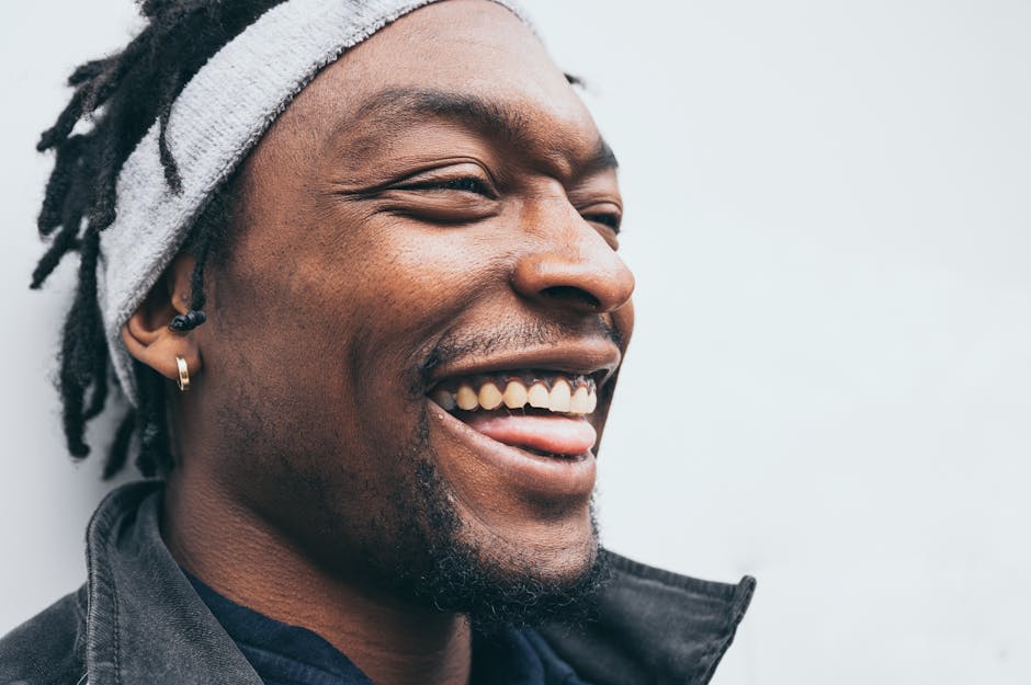 Close-up portrait of a happy man with dreadlocks and earrings wearing a headband, smiling broadly.
