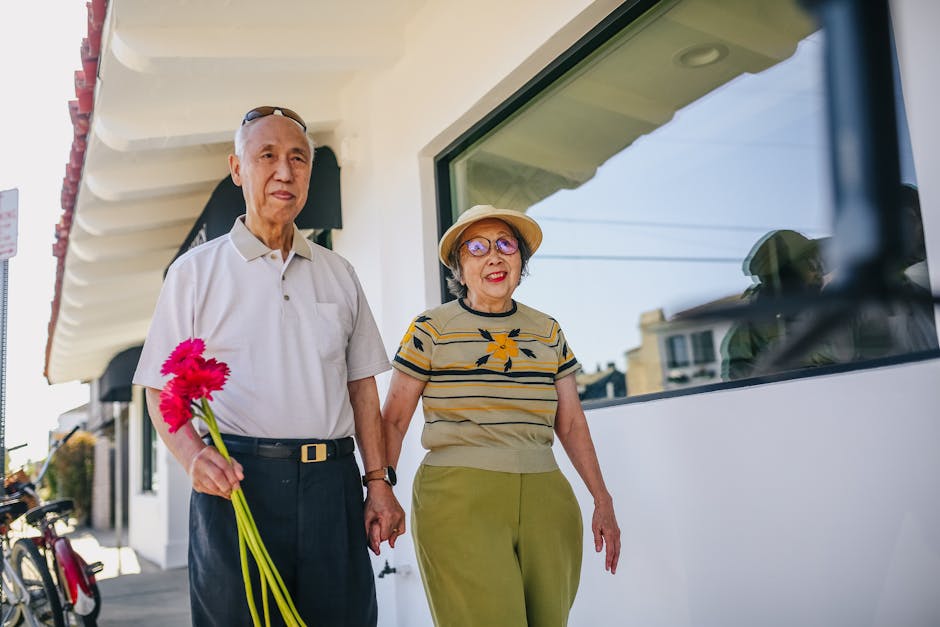 An elderly Asian couple walking hand-in-hand outdoors, enjoying a sunny day.
