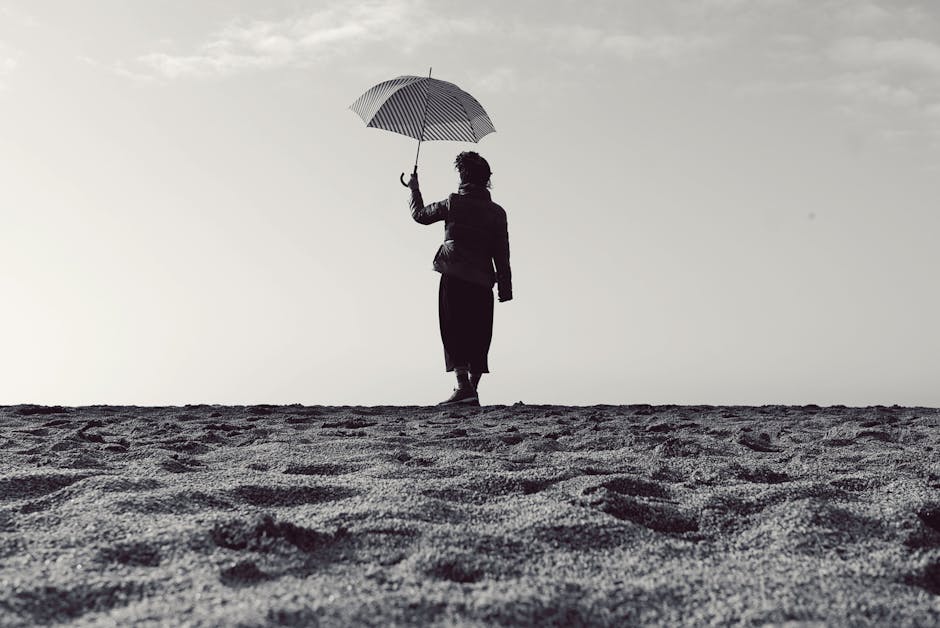 Black and white silhouette of a woman holding an umbrella while standing on a serene beach.
